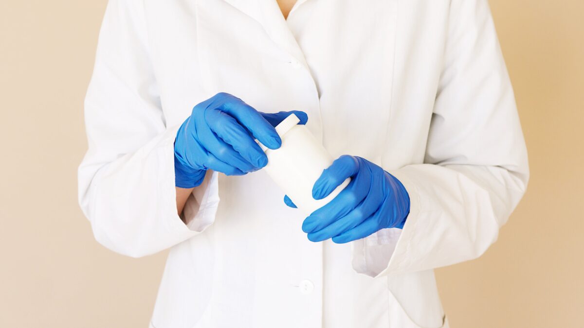 Doctor in white lab coat wearing gloves and holding prescription.