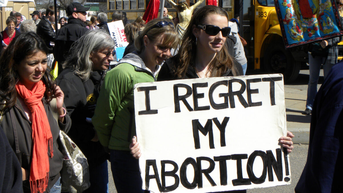 woman carrying sign that says "I regret my abortion" at abortion protest