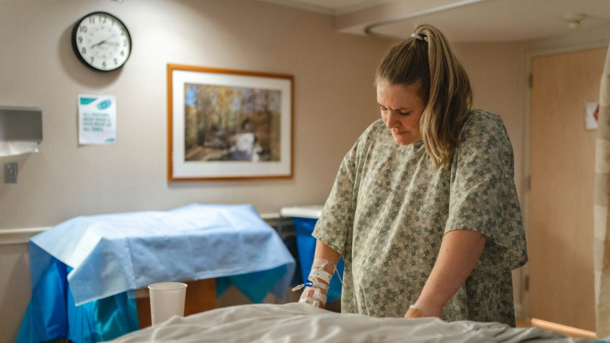 pregnant woman standing next to hospital bed in medical gown