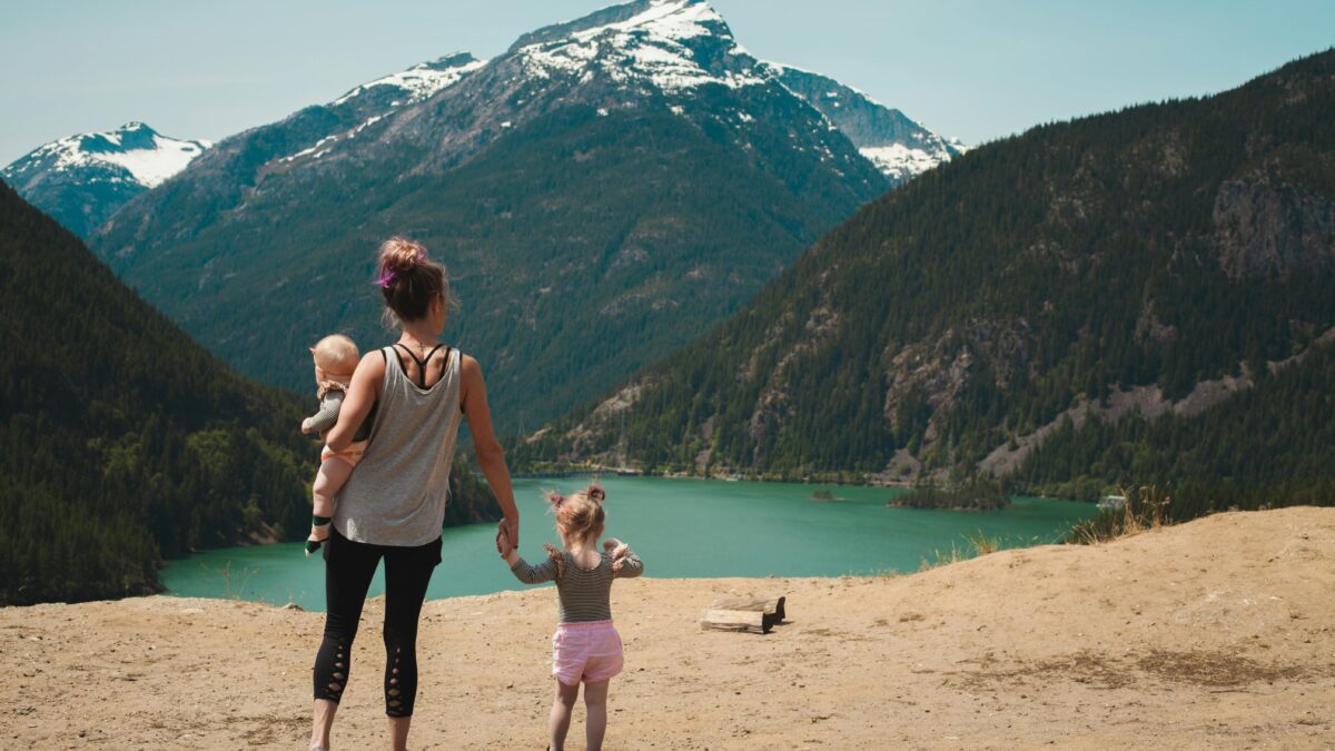 Mother holds one child by the hand and the other in her arm while taking in a view of the mountains.