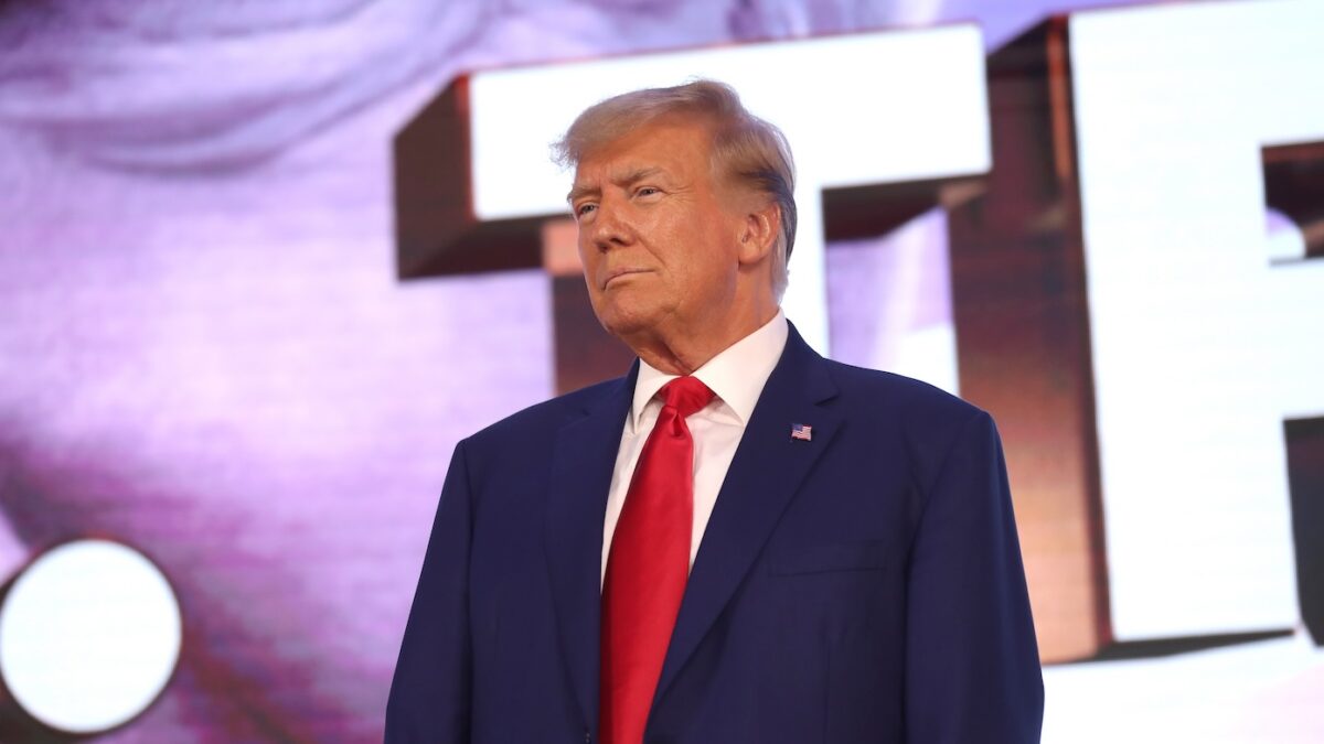 Donald Trump stands in front of purple background