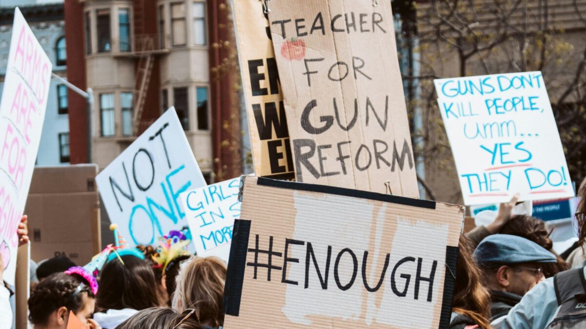 Boy stands in front of adults holding signs at anti-gun protest.