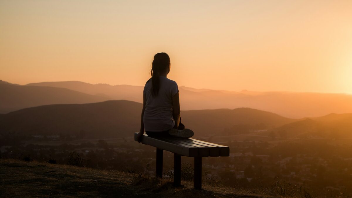 Woman sitting on bench overlooking mountain