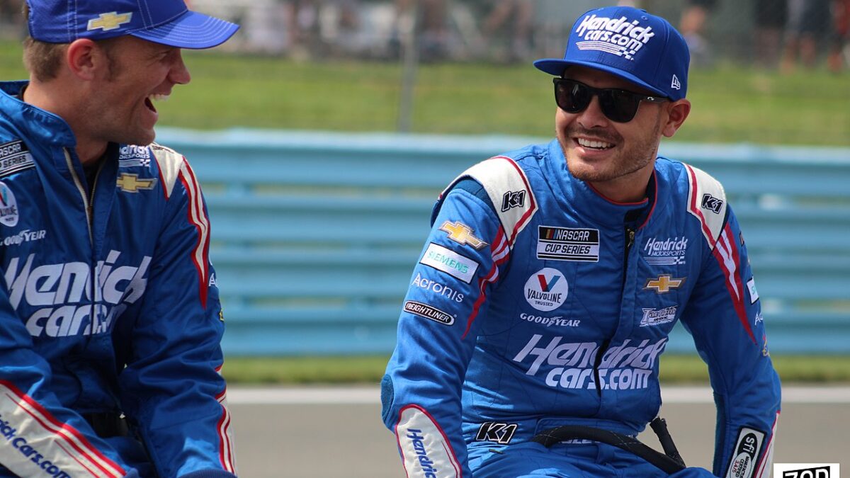 Kyle Larson and another race car driver sitting by track laughing