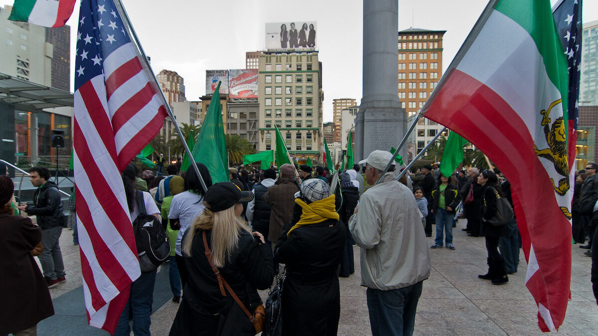 A woman is walking with an American flag and a man is walking with an Iranian flag.