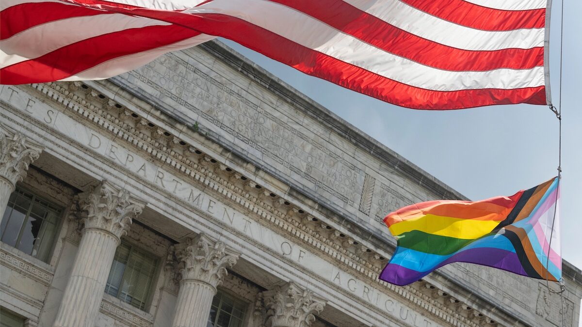 An American flag and a pride flag are flying in front of the Department of Agriculture.