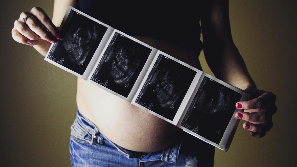 woman holding ultrasound pictures in front of pregnant belly