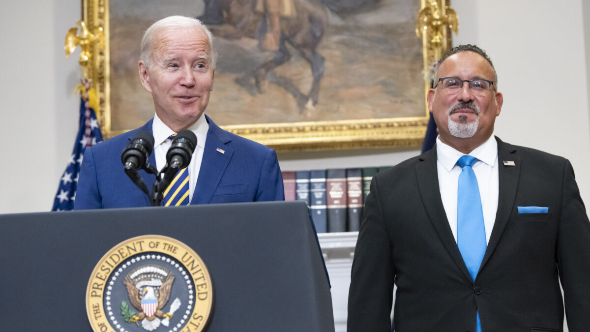 Joe Biden and Miguel Cardona stand behind podium