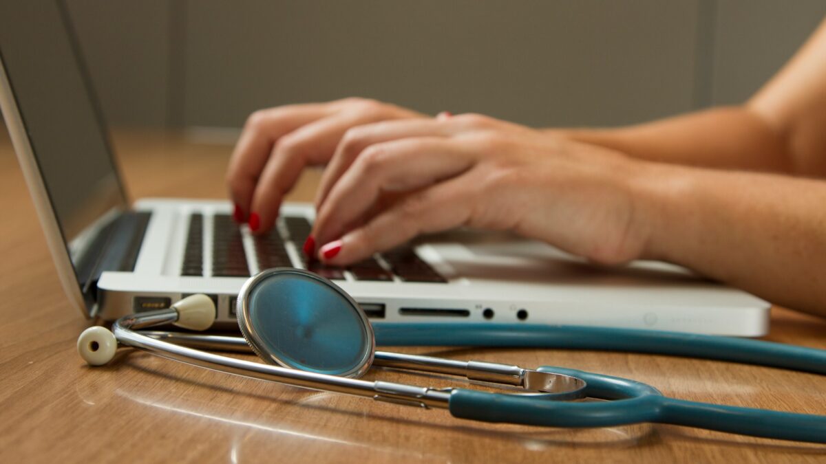 woman typing on laptop next to stethoscope