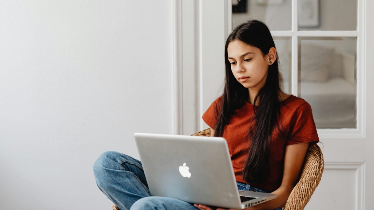 A teen girl sitting a chair using a laptop computer.
