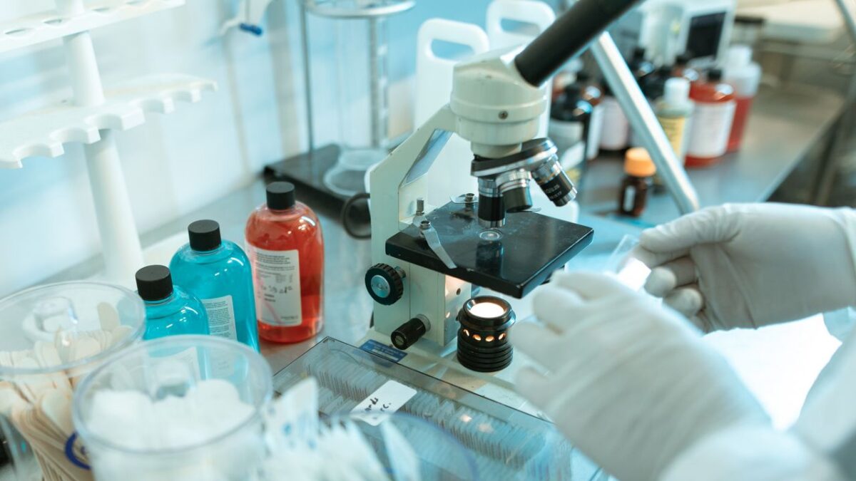 scientist holds a slide next to a microscope